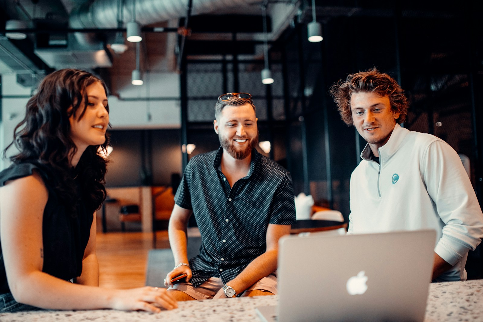 Three young adults in smart casual clothing collaborating around a laptop; illustrative stock photography